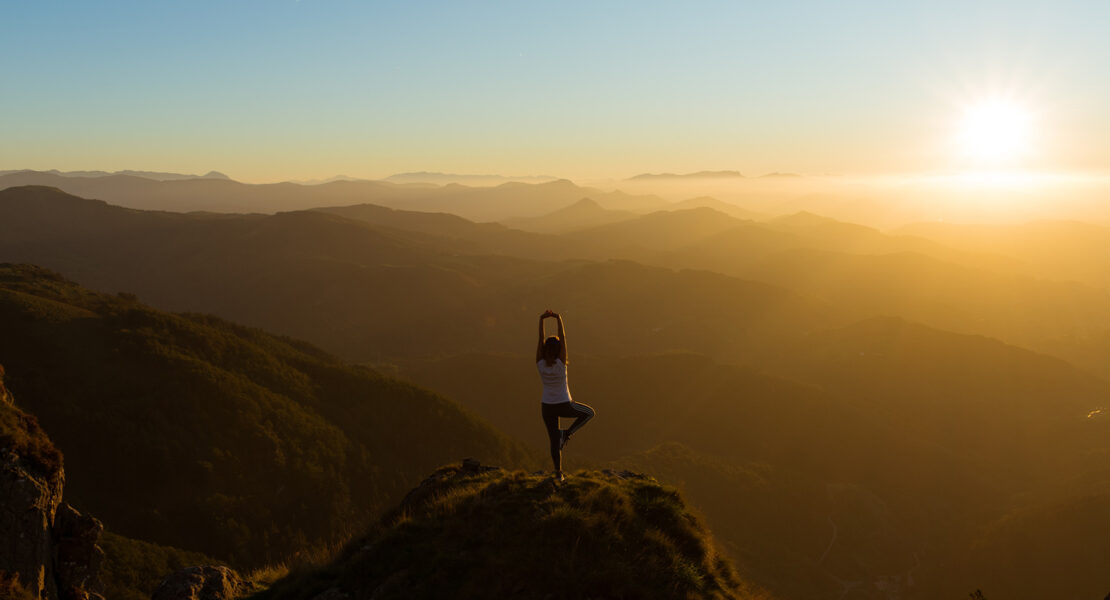 Frau macht Yoga auf einem Berg bei Sonnenuntergang