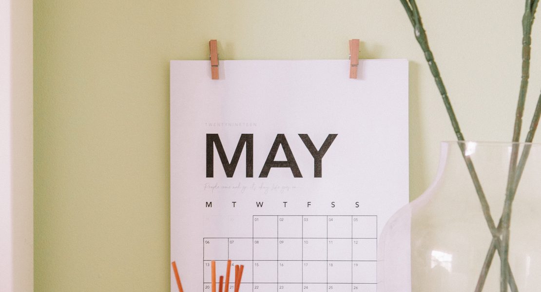 Weißes Kalenderblatt des Monats Mai an einer gelben Wand, davor eine Vase mit Blumen