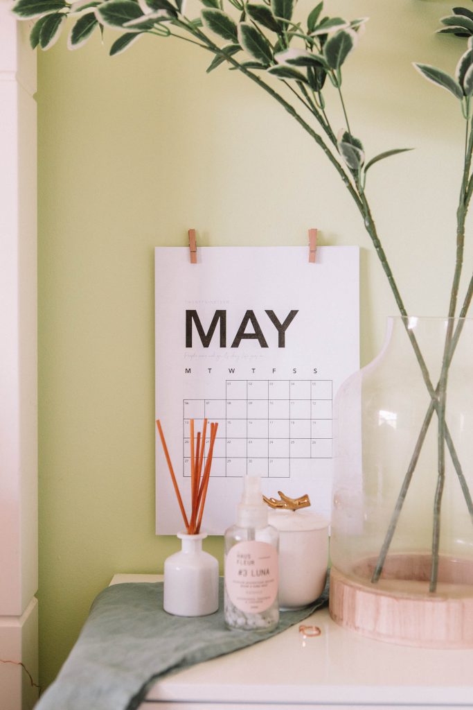 Weißes Kalenderblatt des Monats Mai an einer gelben Wand, davor eine Vase mit Blumen